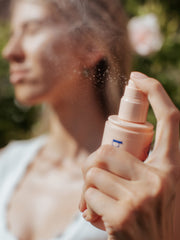A woman is about to drench herself in hydration with Bloom and Blossom's Get Drenched Hydrating Face and Body Mist. She's holding the spray bottle up to her face, ready to give herself a refreshing mist.