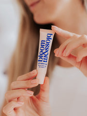 Woman holding tube of Nourishing lip balm, ready to apply to lips to hydrate and nourish.