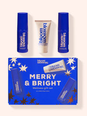 A blue and rose gold starry gift box containing a wellness gift set from Bloom and Blossom. The box features the text "Merry & Bright" and "Wellness Gift Set" in bold white lettering. Inside, there are four smaller blue bottles and tubes labeled with the brand name and product descriptions like "Wonder Worker", "Pyjamarama" and "All Night Long." The overall design is festive and cheerful.