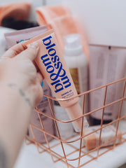 Picking up a tube of Hands Up Age-defying hand cream from a basket full of essential skincare products.